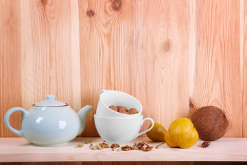 Teapot with cups, nuts and pears on wooden background