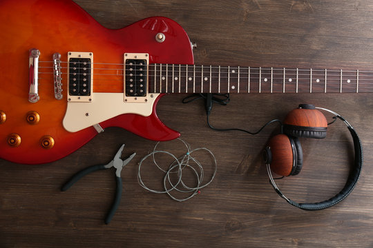 Electric guitar with headphones, pliers and strings on wooden background