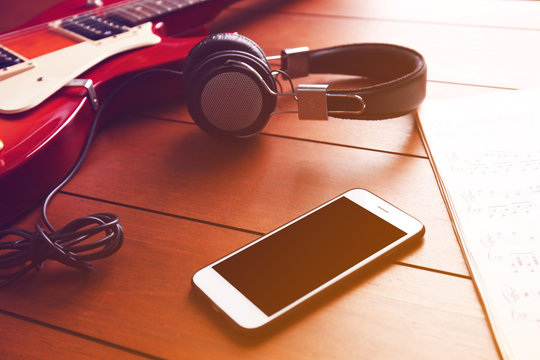 Electric guitar with headphones and mobile phone on wooden background