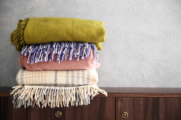 Stack of warm plaids on wooden commode over grey wall background