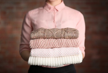 Stack of knitted clothes in female hands on blurred wall background