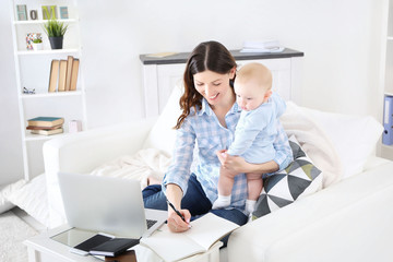 Beautiful woman with baby boy working from home using laptop