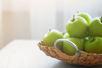 Ripe green apples in a wicker basket on a kitchen table