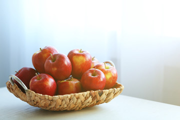 Ripe red apples in wicker basket on a kitchen table