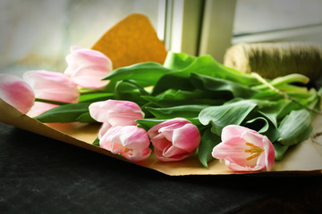 Bouquet of pink tulips on wrapping paper over black wooden windowsill