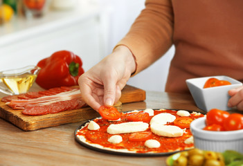 Woman making a pizza on a wooden table, close up