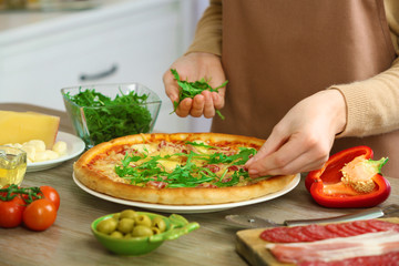 Obraz na płótnie Canvas Woman decorating fresh baked pizza with arugula, close up