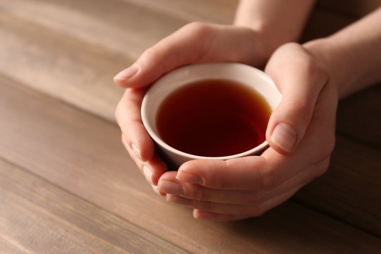 Female hands holding cup of tea on wooden background