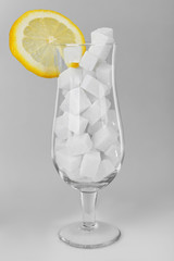 Hurricane glass with lump sugar and slice of lemon on grey background