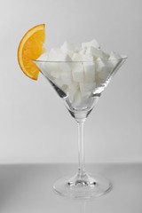 Martini glass with lump sugar and slice of orange on grey background