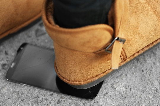 Female boots crushing a mobile phone on the pavement