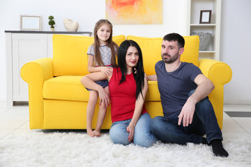 Obraz premium Parents and their daughter sitting on the floor beside yellow sofa.