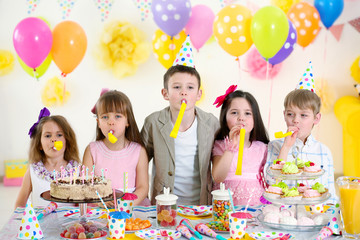 Happy group of children with yellow noise makers having fun at birthday party