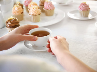 Female hands at the table with tea and cupcakes closeup