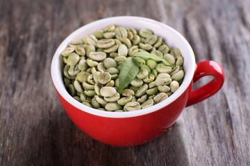 Green coffee beans in a red cup on wooden table