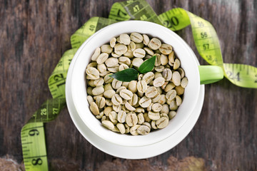 Green coffee beans in a cup with measuring tape on wooden table