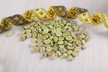 Green coffee beans with measuring tape on white wooden table