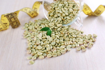 Green coffee beans in a cup with measuring tape on white wooden table