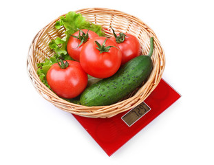Basket with fresh vegetables on digital kitchen scales, isolated on white