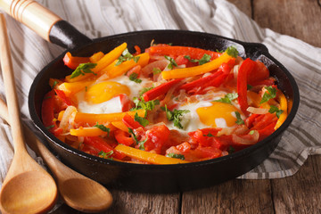 Tasty Piperade: fried eggs with peppers and tomatoes close up in a pan
