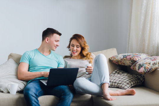 Young couple lying on couch, man using laptop computer.