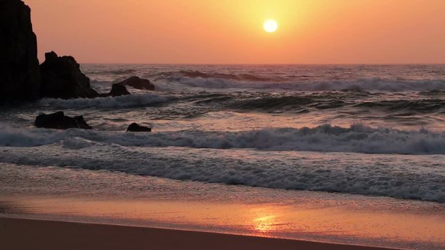 Sandy beach and rock. The ocean surf and the sunset over the infinite ocean. Slow motion