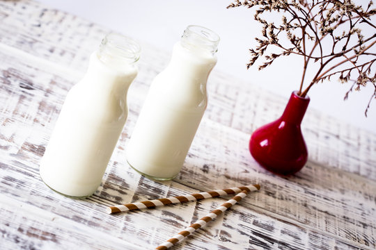 Two bottles of milk with striped straws standing on old table.