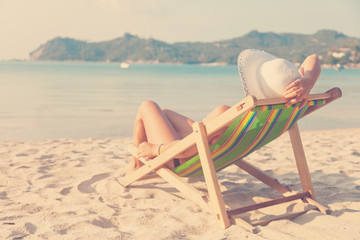 woman in a hat on a beach, sitting in a deck chair and watching