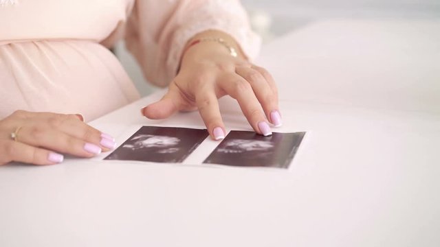 Close up of  pregnant touching ultrasound pictures of baby at the table. 4k