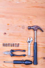 Essential basic tools set consisting hammer, plier, screwdriver and adjustable crescent on wooden background