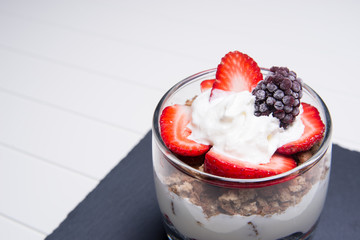 Traditional English dessert strawberry trifle with blackberries in a transparent glass on the slab of slate on a white background