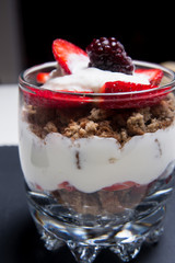 Traditional English dessert strawberry trifle with blackberries in a transparent glass on a plate of slate