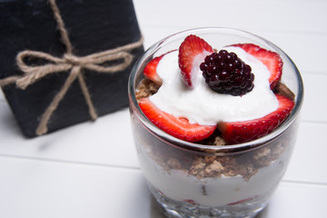 Traditional English dessert strawberry trifle with blackberries in a transparent glass on a white background with a gift of a plate of slate