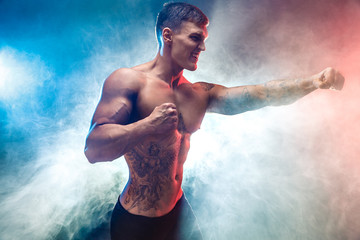 Muscular  fighter punching in smoke. Colour background.