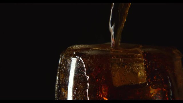 A cola drink are pouring in glass with ice on a black background