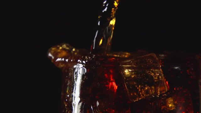 SLOW: A cola drink are pouring in glass with ice on a black background