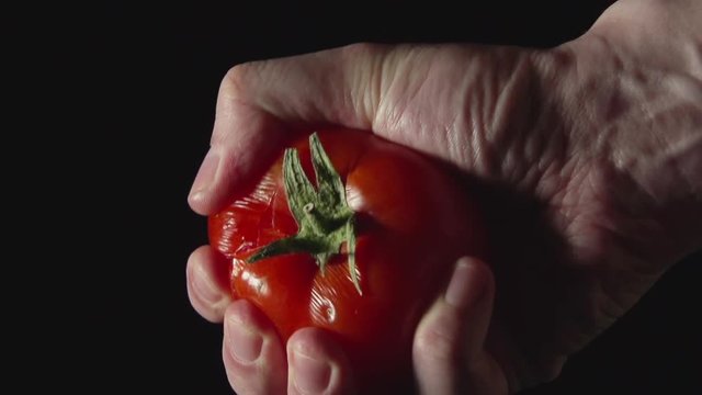 Man hand presses a tomato on a black background