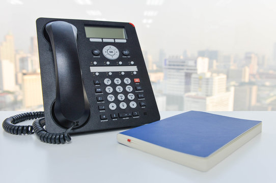IP Phone and blue notebook on the white table - Technology of communication