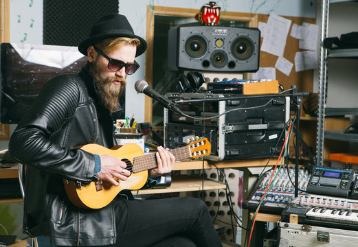 Hipster man singing and playing guitar in a studio