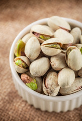 Pistachios in white ceramic jar on rustic fabric background