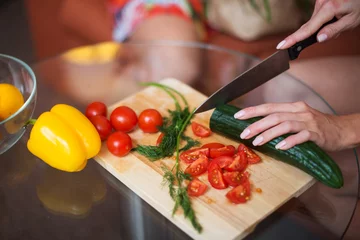 Fotobehang close-up woman cutting tomatoes vegetable salad on a wooden board in the kitchen © undrey