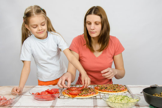  Six-year girl helps mother spread on tomato pizza
