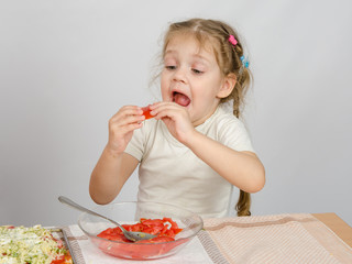 A little girl tries to stick to widely open mouth large slice of tomato
