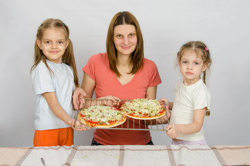 Obraz na płótnie Canvas Mom and two small daughters show the two had not yet made baked pizza on a baking sheet