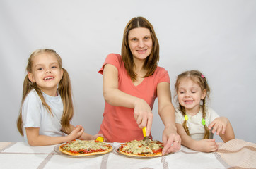 Mother and two little daughters happy sitting at a table with two pizzas