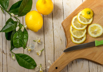 Несколько спелых лимонов украшенных листьями цветущего лимонного дерева на деревянном фоне