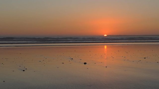 Only part of sun is left above horizon at the sunset.Orange sunlight reflection on wet flat beach sand.Great travel,beach background with plenty of copy space.