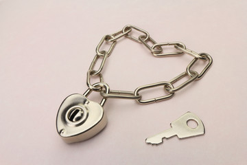 Heart shaped padlock and chain with key on a pink paper background