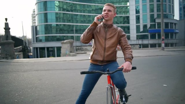young male bicyclist talks on the phone in downtown slow motion