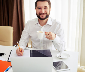 Smiling man working and drink a coffee in the white office
